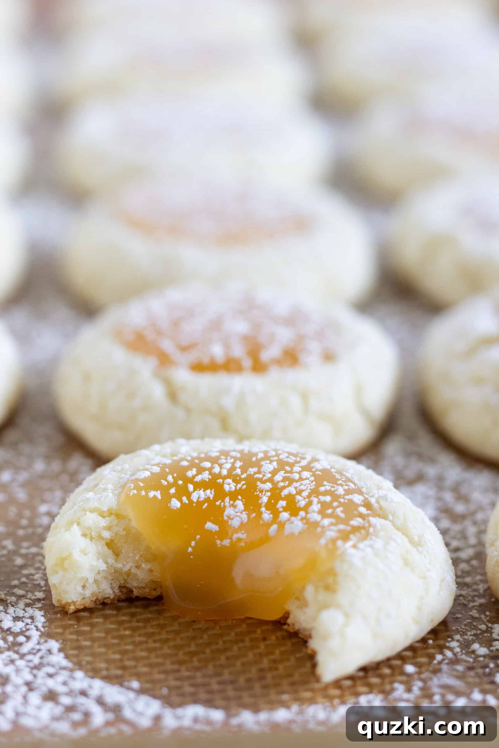 7 Effortless and Amazing Thumbprint Cookies 4 A baking sheet is filled with perfectly baked Lemon Curd Thumbprint Cookies, lightly dusted with powdered sugar, with one cookie showing a delicate bite taken out of it.