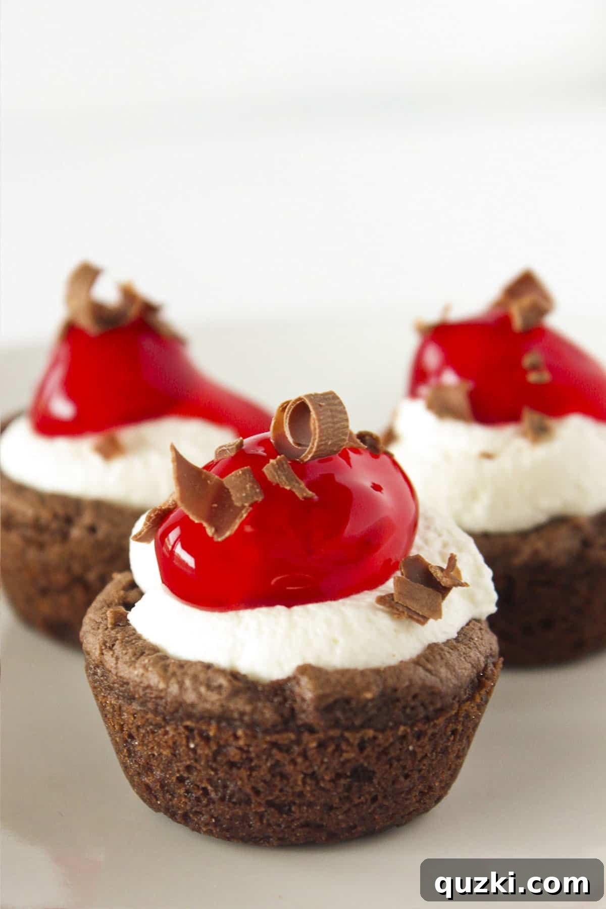 20 Festive Cake Mix Cookies Made Easy 17 An elegant trio of Black Forest Cookie Cups, each filled with whipped cream and cherries, beautifully presented on a white plate.