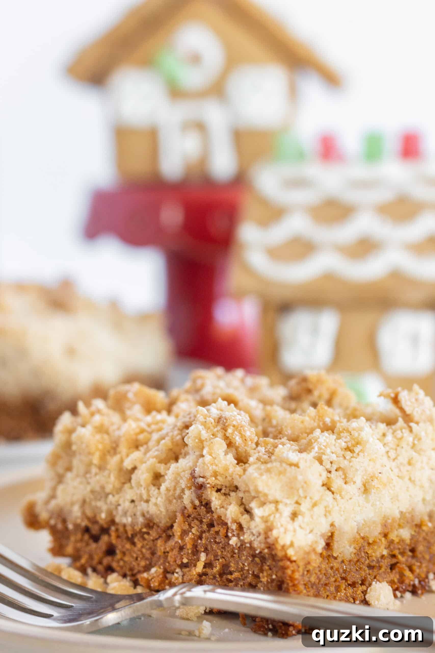 Simple Spiced Gingerbread Coffee Cake 3 Two generous slices of Gingerbread Crumb Coffee Cake are presented on white plates, ready to be served. In the softly blurred background, miniature gingerbread houses add a festive holiday touch.