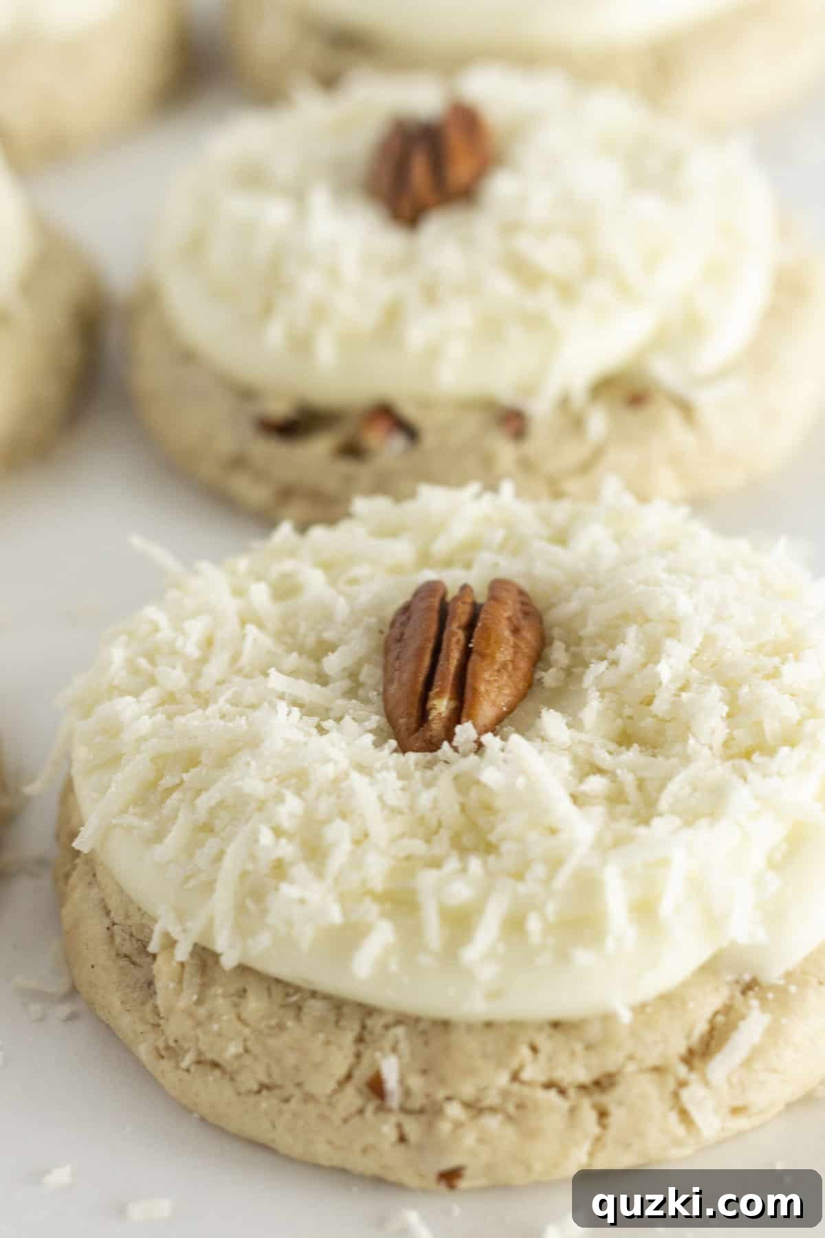 A close up photo of a half dozen coconut pecan cookies with coconut and a pecan on top. Each cookie is generously frosted and garnished, showcasing its irresistible texture and topping.