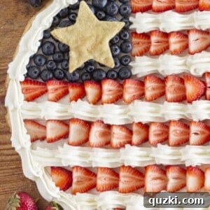 A round flag fruit pizza with fresh strawberries and blueberries arranged in a patriotic design.