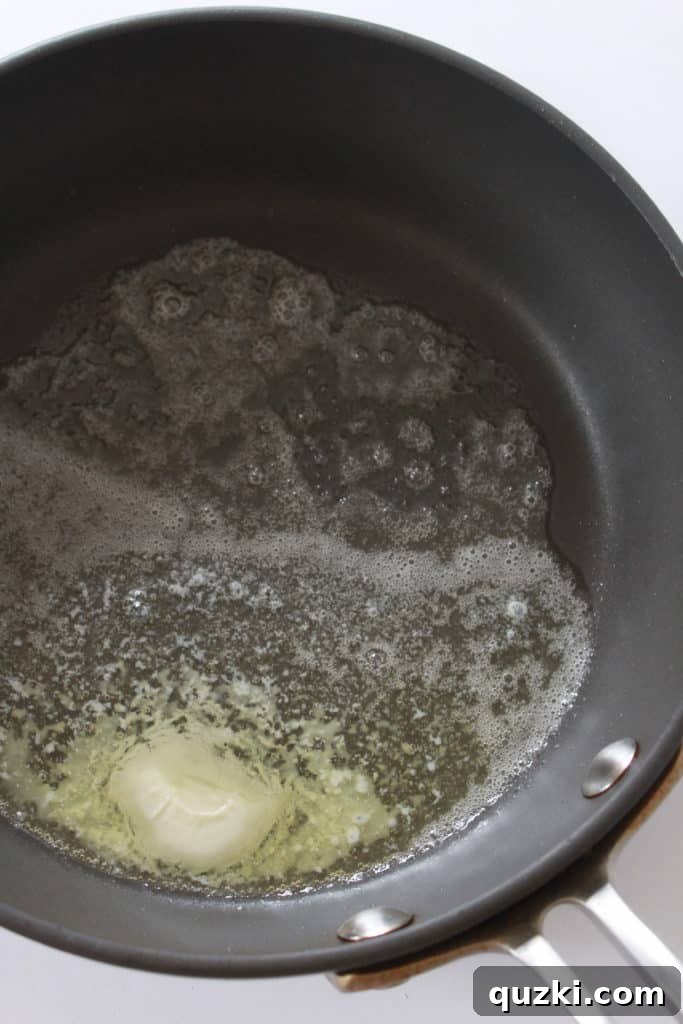 Fresh corn kernels being sautéed in a skillet with butter, beginning to develop a golden-brown color.