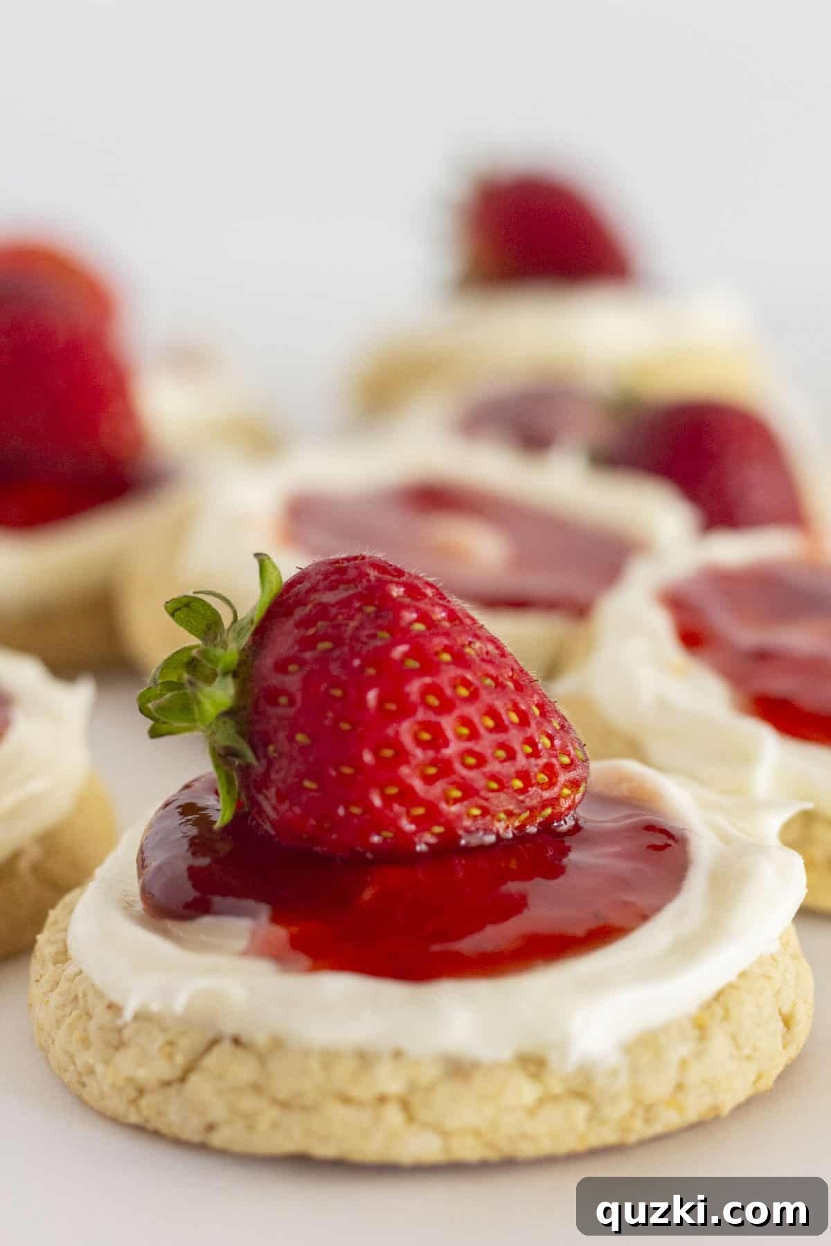 A dozen Strawberry Cheesecake Cookies artfully arranged with fresh strawberries on top, showcasing the creamy frosting and rich jam center.