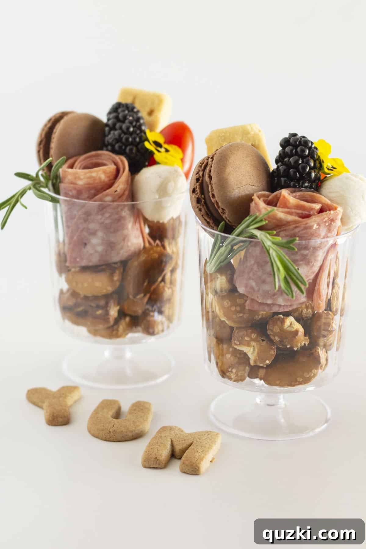 Two individual charcuterie cups in clear cups featuring beautifully arranged salami roses, cheese, and fruit.