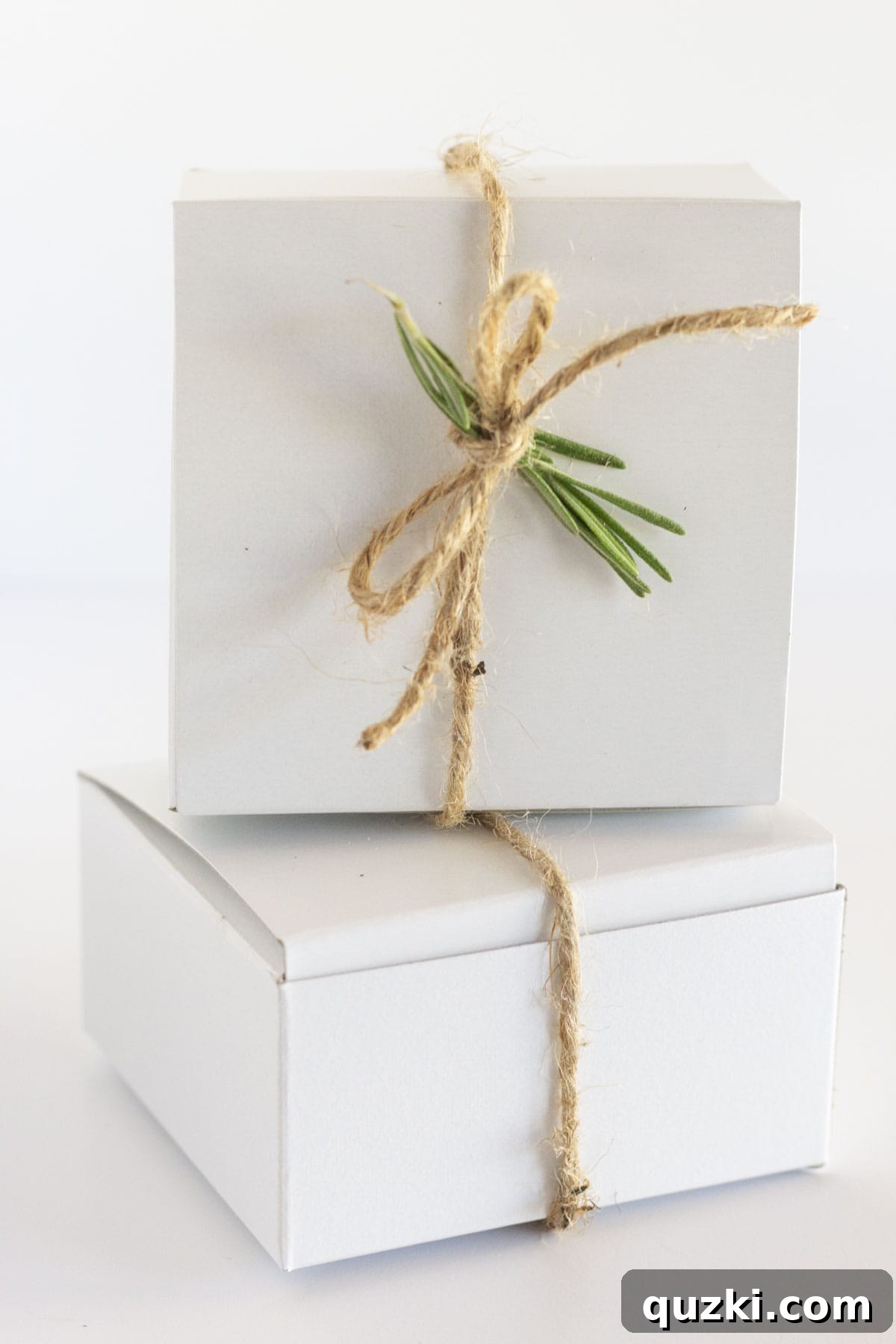 Two charcuterie boxes tied with jute string and adorned with fresh rosemary, ready for distribution.