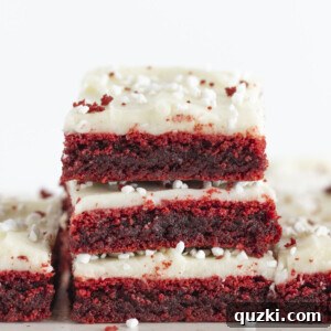 Three red velvet brownies with cream cheese frosting stacked on each other.