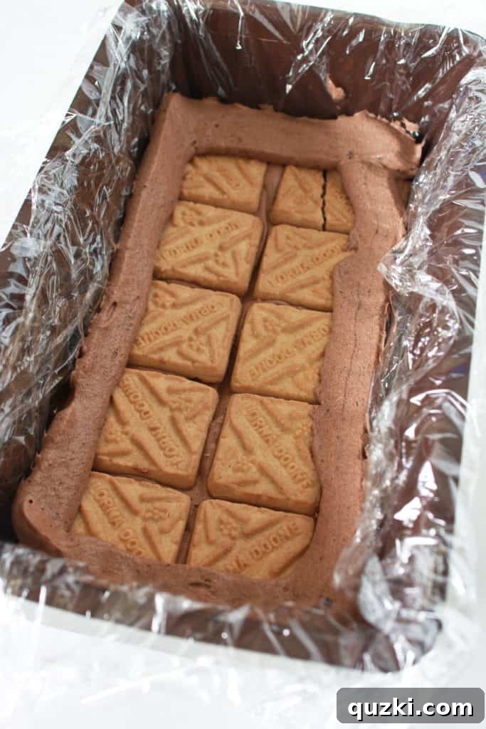 Carefully placing a layer of golden shortbread cookies over the initial chocolate pudding base, then piping a precise pudding ring along the edges to prepare for the caramel layer in the Twix Icebox Cake.
