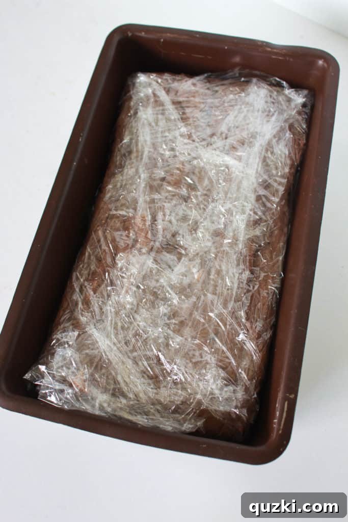 The assembled Twix Icebox Cake, meticulously wrapped in plastic film, ready for its essential journey into the freezer to set and solidify for ultimate flavor and texture.