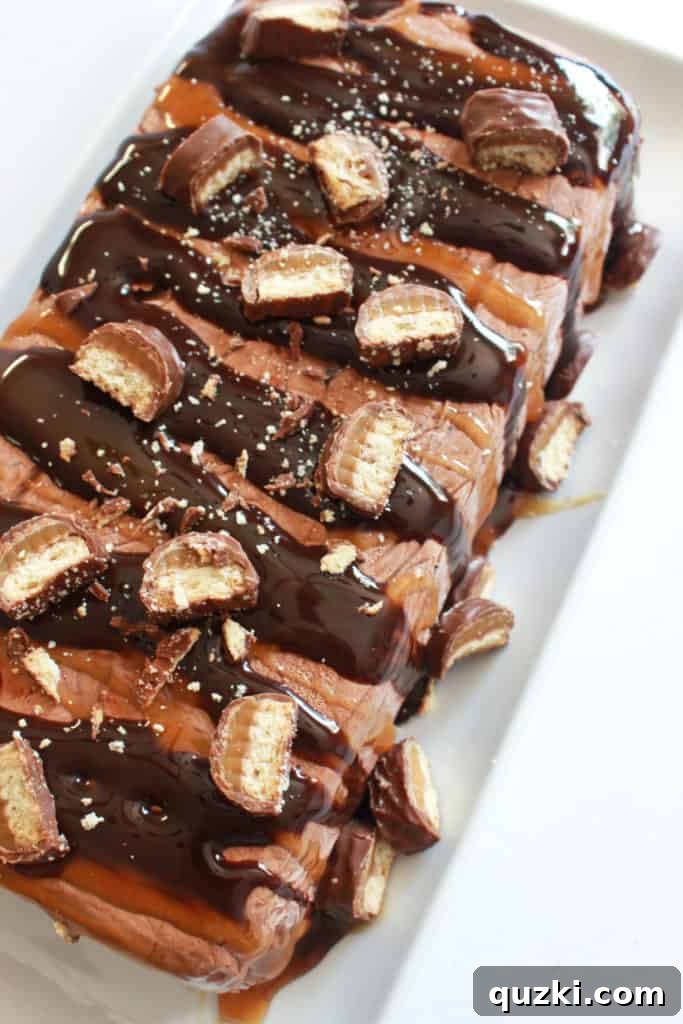 A beautifully garnished Twix Icebox Cake, freshly removed from its pan, expertly drizzled with rich chocolate syrup and luscious caramel sauce, then topped with delightful pieces of chopped Twix candy bars, ready for serving.