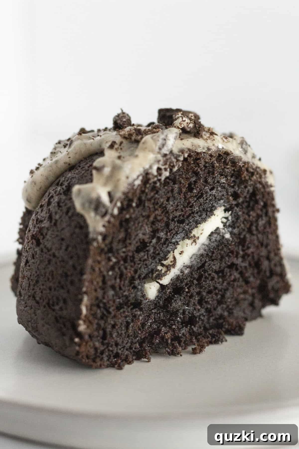 A perfectly portioned slice of Oreo Bundt Cake sitting on a elegant white plate, drizzled with glaze and topped with cookie crumbs.