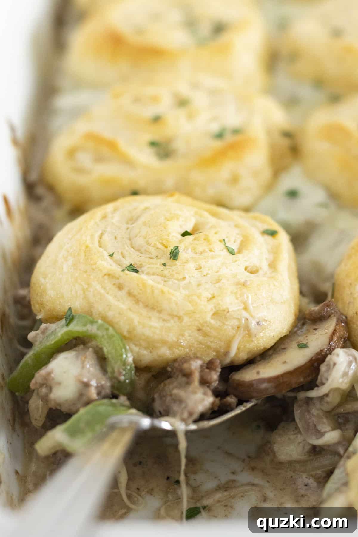 Ultimate Philly Cheesesteak Bake 2 Serving a spoonful of Philly Cheesesteak casserole with crescent roll top.