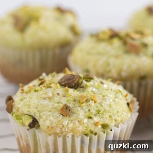 Pudding Mix Perfection: Effortless Pistachio Muffins 8 Pistachio muffins on a wire rack with pistachios and sanding sugar on top.
