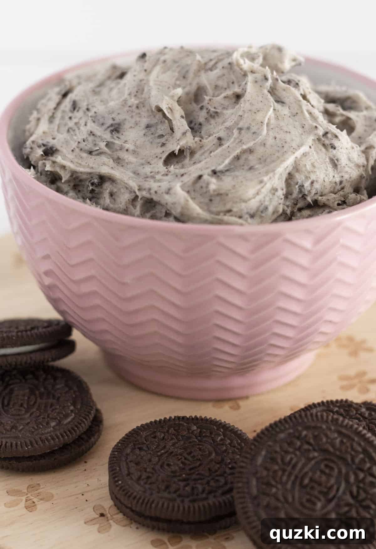 Cookies and cream frosting in a pink bowl with Oreo cookies around it.