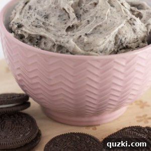 Cookies and cream frosting in a pink bowl with Oreo cookies around it.