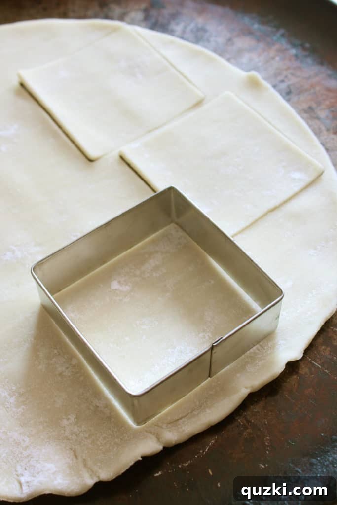 Unrolled refrigerated pie dough being precisely cut into squares using a cookie cutter on a lightly floured surface, preparing for the peach filling.