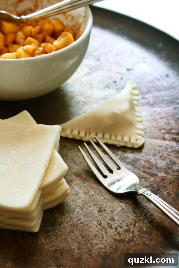 The edges of a peach turnover being meticulously crimped with a fork to create a secure, decorative seal, preventing filling from escaping.