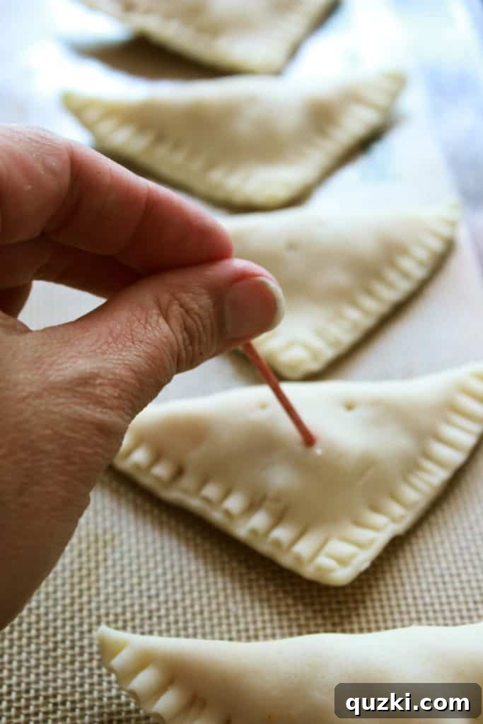 Close-up of a peach turnover on a baking sheet, featuring small holes poked on its surface with a toothpick to allow steam to escape during baking, ensuring a perfect crust.