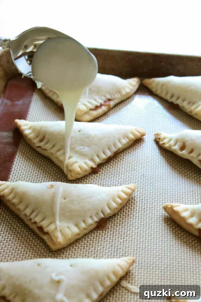 Freshly baked peach turnovers, still warm, being expertly drizzled with a smooth vanilla glaze and then sprinkled with an alluring cinnamon sugar mixture.