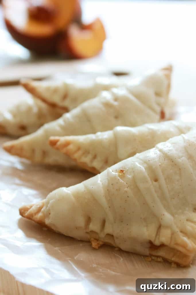 A beautifully arranged stack of finished fresh peach turnovers on a pristine white plate, showcasing their perfect golden crust and inviting glaze, ready to be enjoyed.