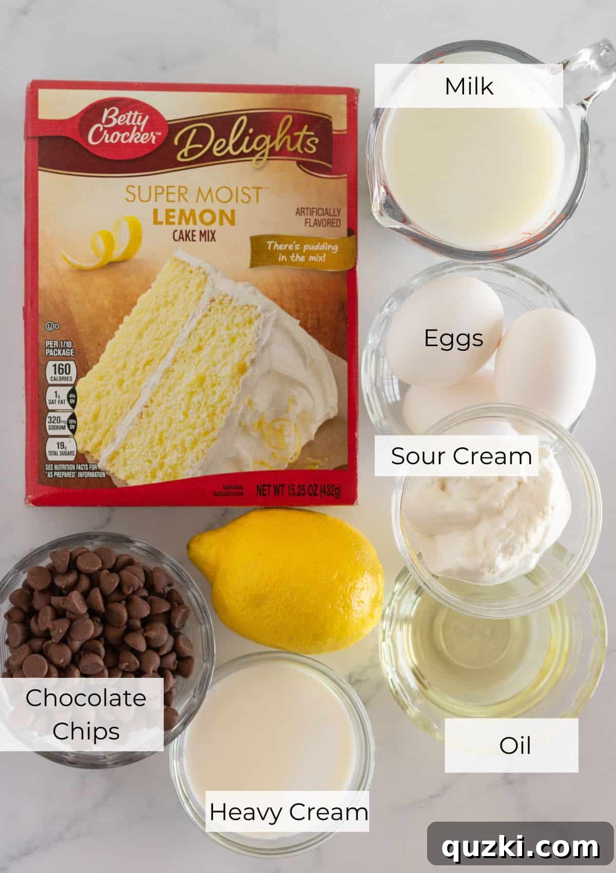 Ultimate Chocolate Lemon Bundt Cake 3 A collection of ingredients laid out on a table, including a box of lemon cake mix, eggs, vegetable oil, milk, sour cream, lemons, milk chocolate chips, and heavy cream, ready for baking.
