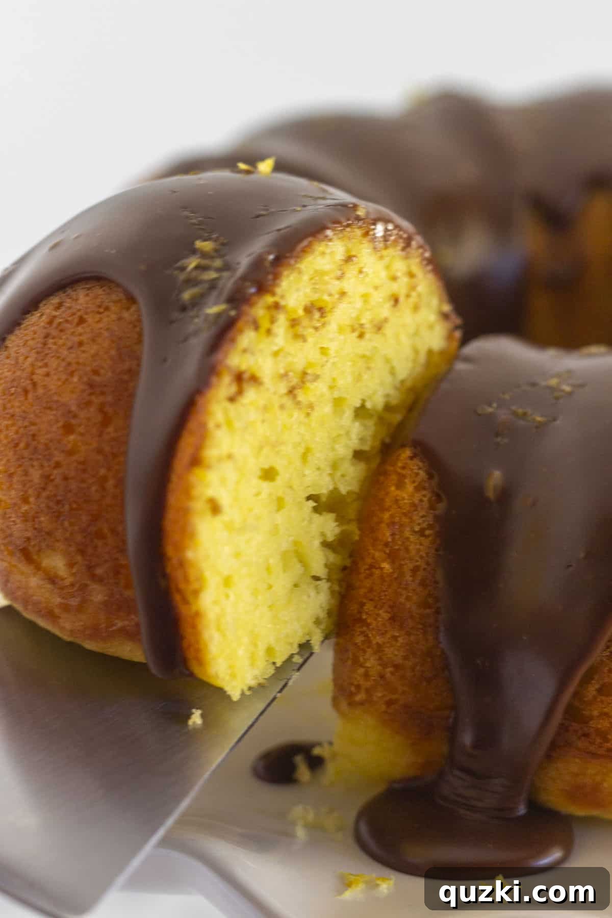 Ultimate Chocolate Lemon Bundt Cake 7 A perfectly portioned slice of lemon cake with chocolate ganache and lemon zest on a white plate, with the remainder of the bundt cake artfully blurred in the background, ready to be enjoyed.