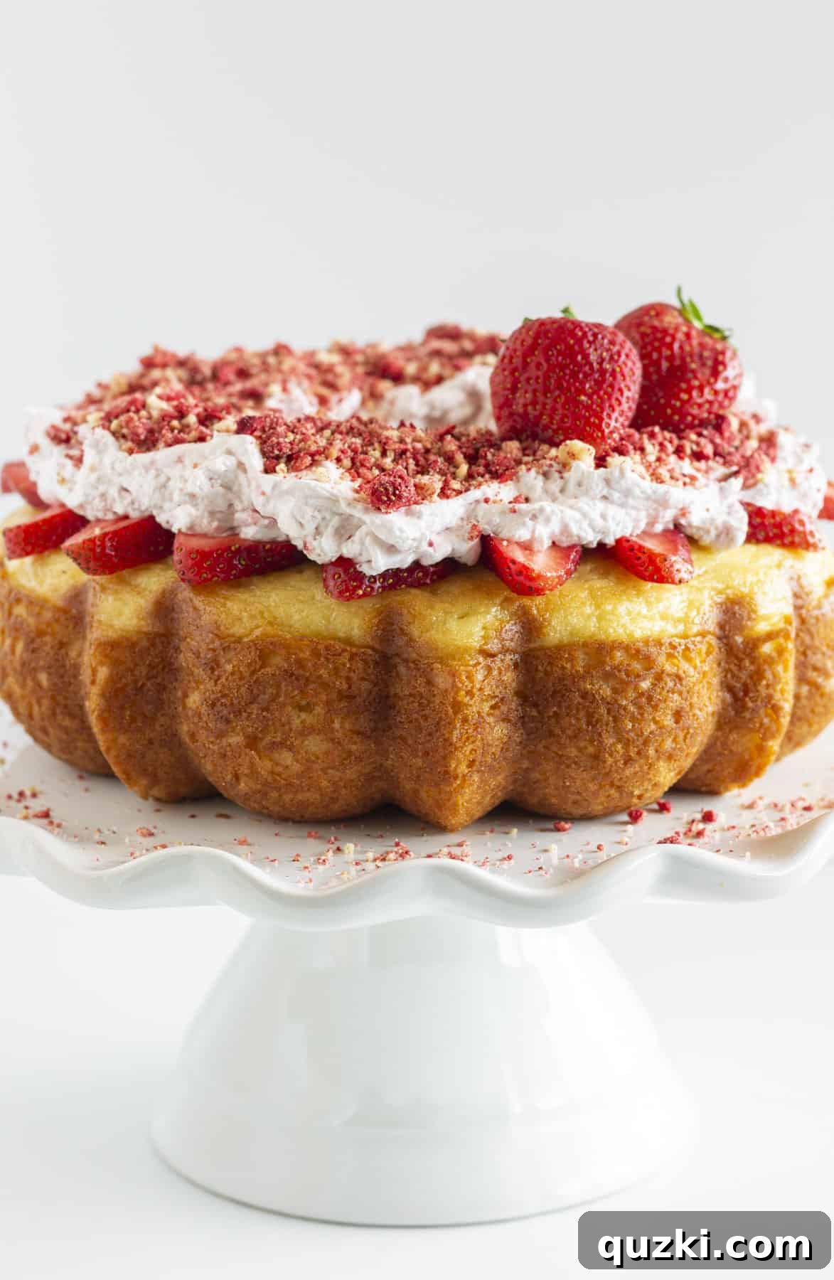A Strawberry Crunch Cake on a white tray, adorned with fresh strawberries and a light drizzle.