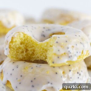 A close-up of a stack of glazed lemon donuts, one with a bite taken out, enticingly showcasing its texture and glaze.