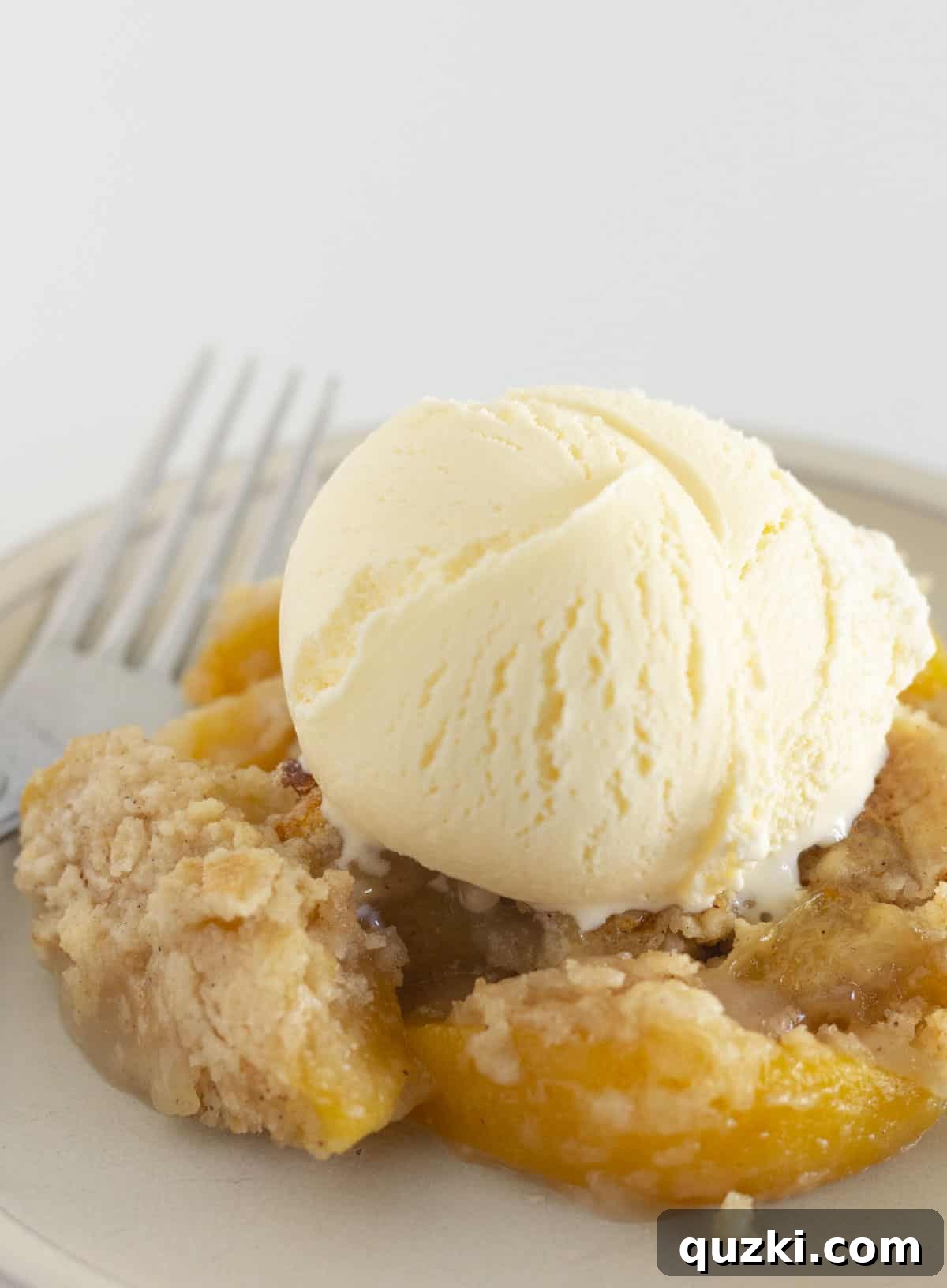 4-Ingredient Effortless Cake Mix Peach Cobbler 5 A serving of peach cobbler made with a cake mix and canned peaches, elegantly topped with a scoop of vanilla ice cream, ready to be enjoyed.
