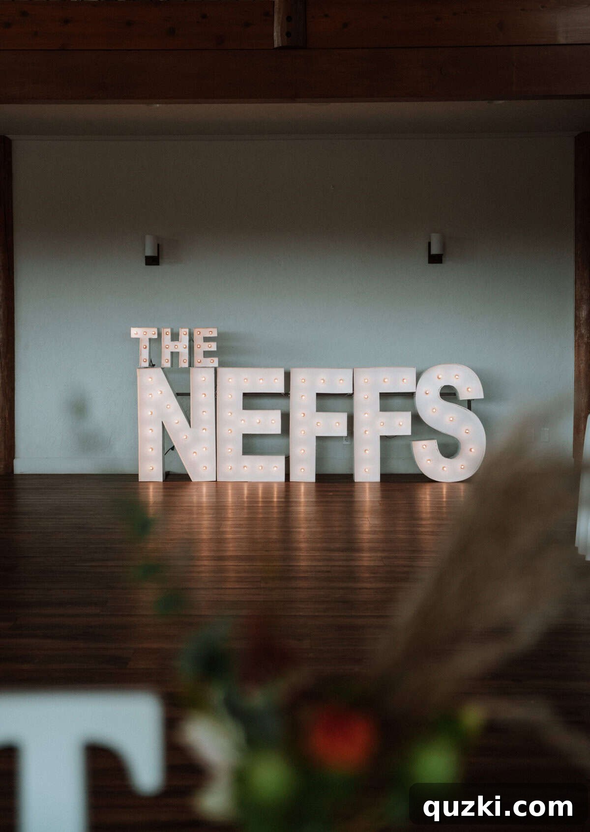 Large, illuminated marquee letters spelling 'The Neffs' on the dance floor, creating a celebratory focal point at the wedding reception.