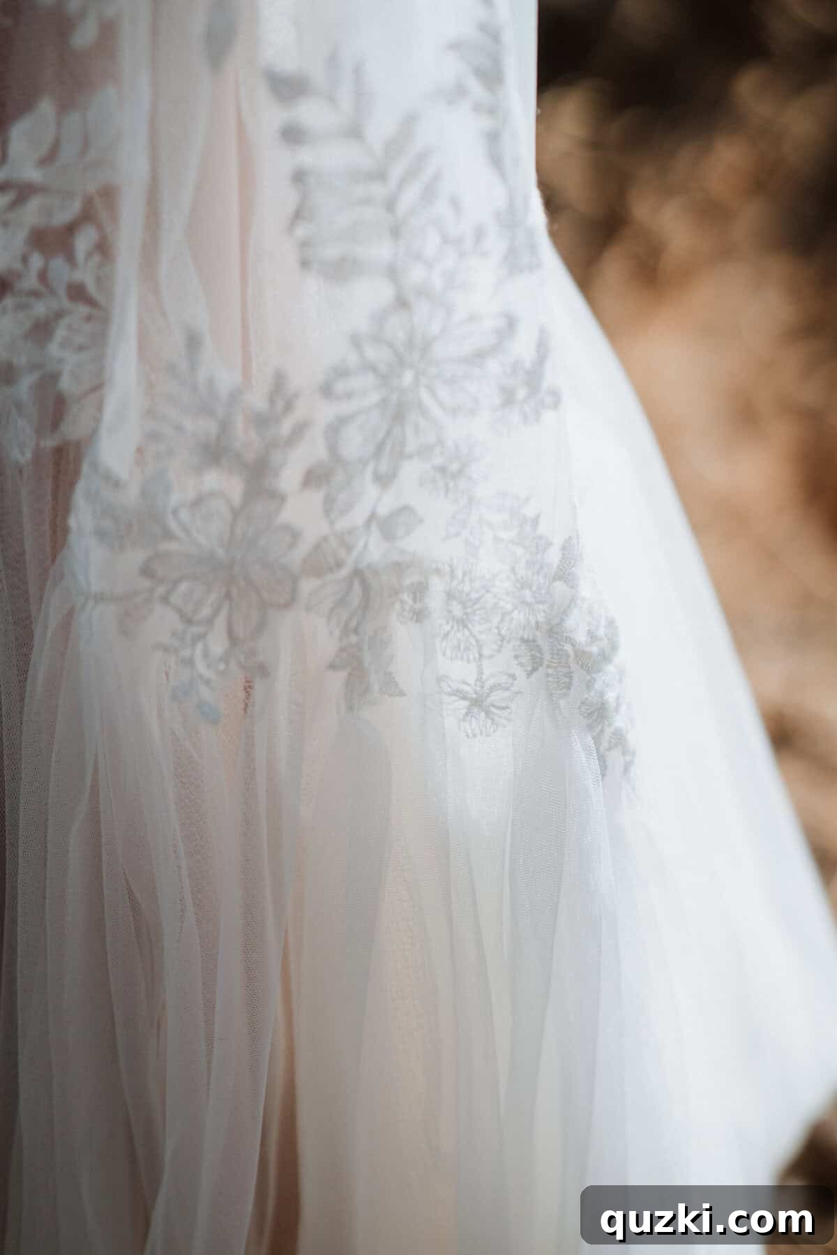 A magnificent close-up shot of the wedding dress, showcasing its intricate tulle and delicate lace details, artfully displayed amongst the branches of trees.