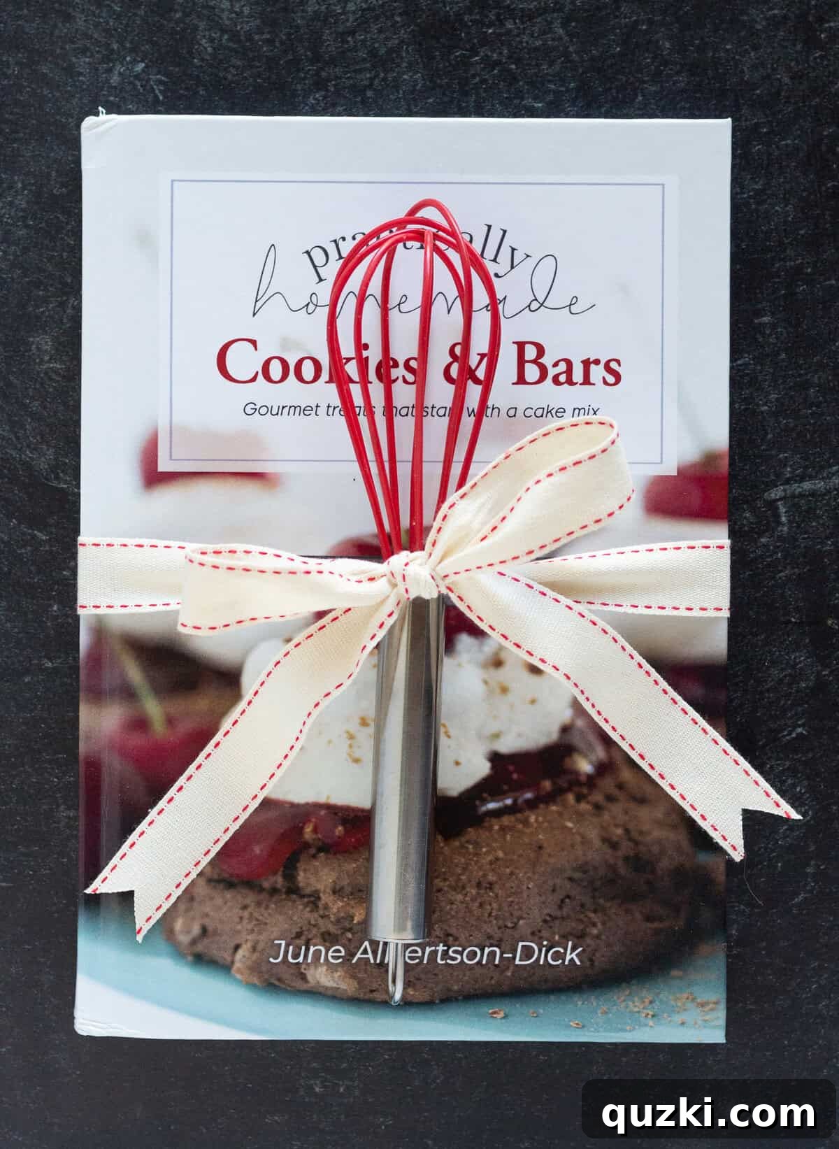 A beautifully presented cookie cookbook elegantly tied with a vibrant ribbon, featuring a high-quality whisk attached, creating an inviting and practical gift ready for use.