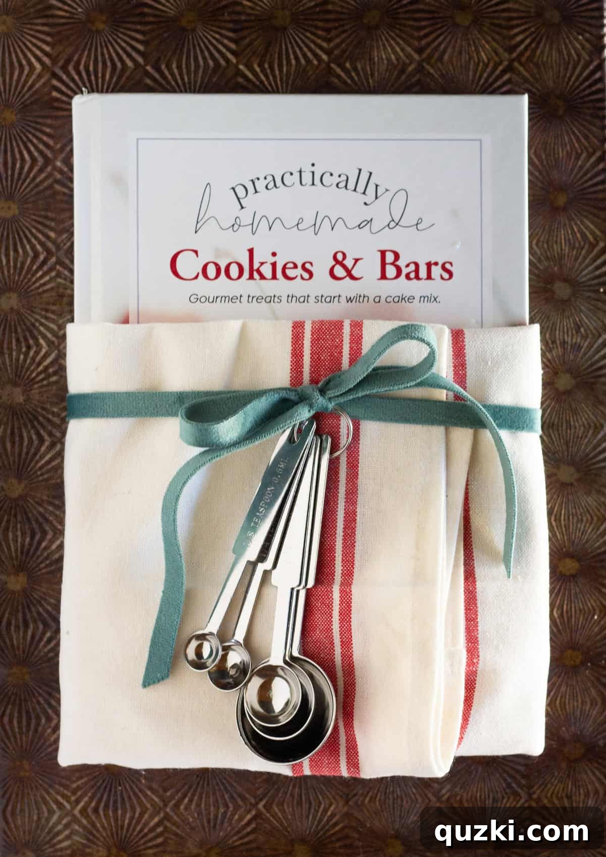 An inspiring cookbook elegantly wrapped in a beautiful tea towel, adorned with a decorative ribbon and a charming set of measuring cups, ready to be gifted.