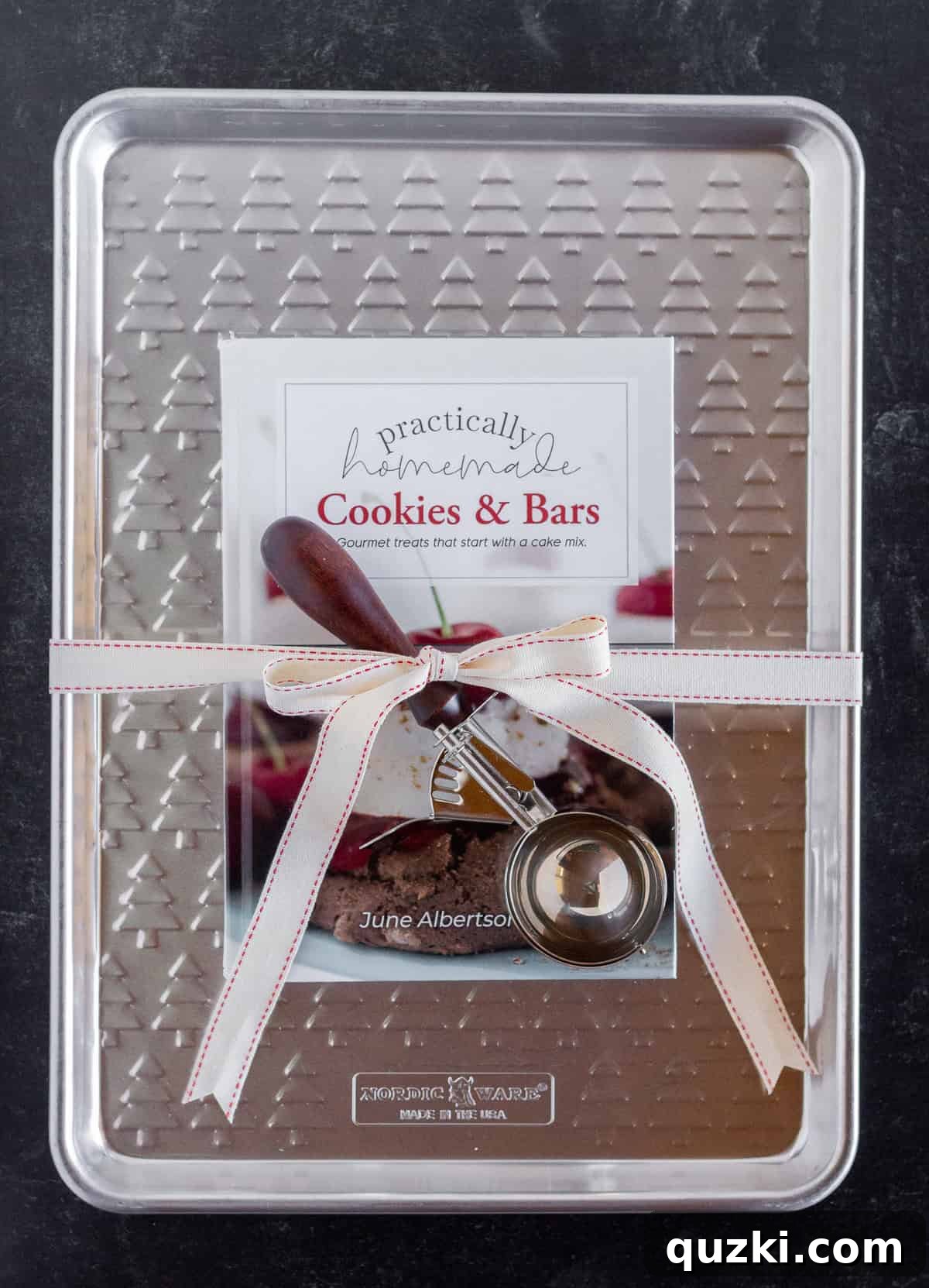 A cookie cookbook thoughtfully arranged on a durable baking sheet, secured with a vibrant ribbon and accompanied by a precise cookie scoop, presenting a complete baking gift set.