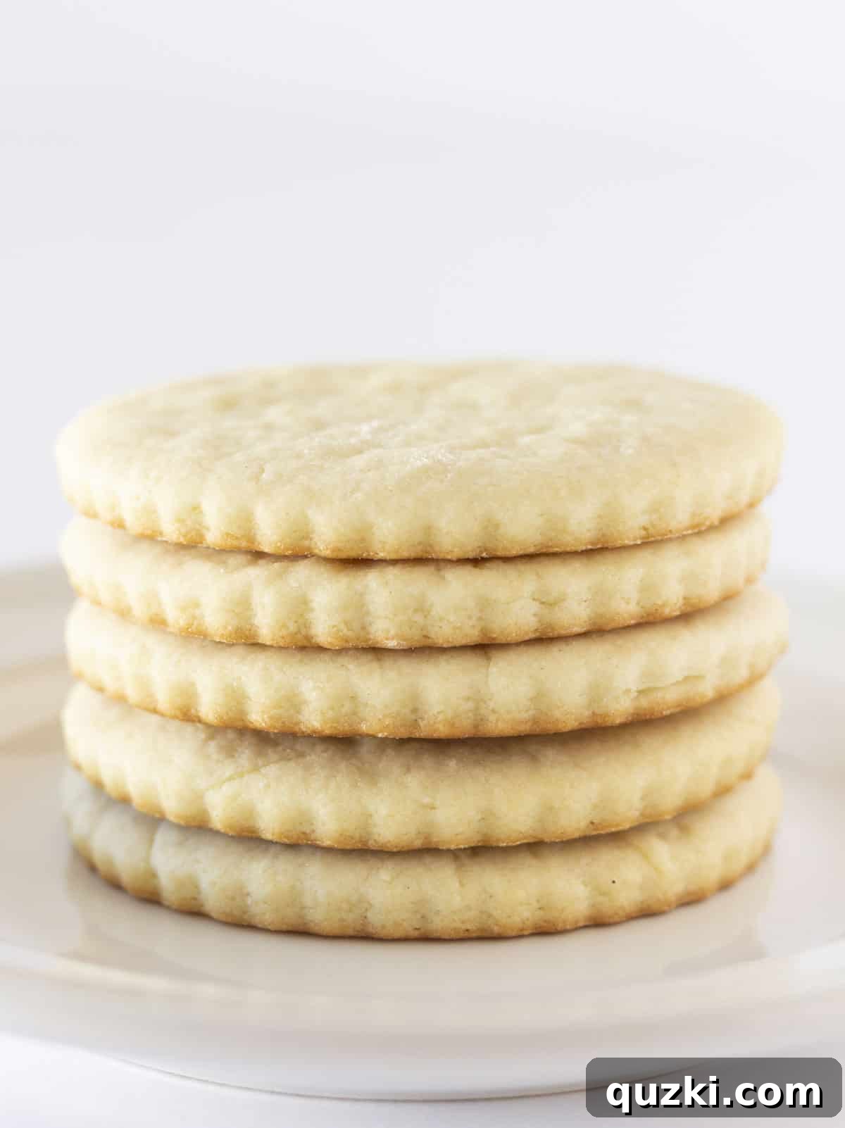 Holiday Cookie Exchange Favorites 7 A stack of beautifully frosted Cream Cheese Sugar Cookies, showcasing their delicate decorations and soft texture, presented on a pristine white plate.