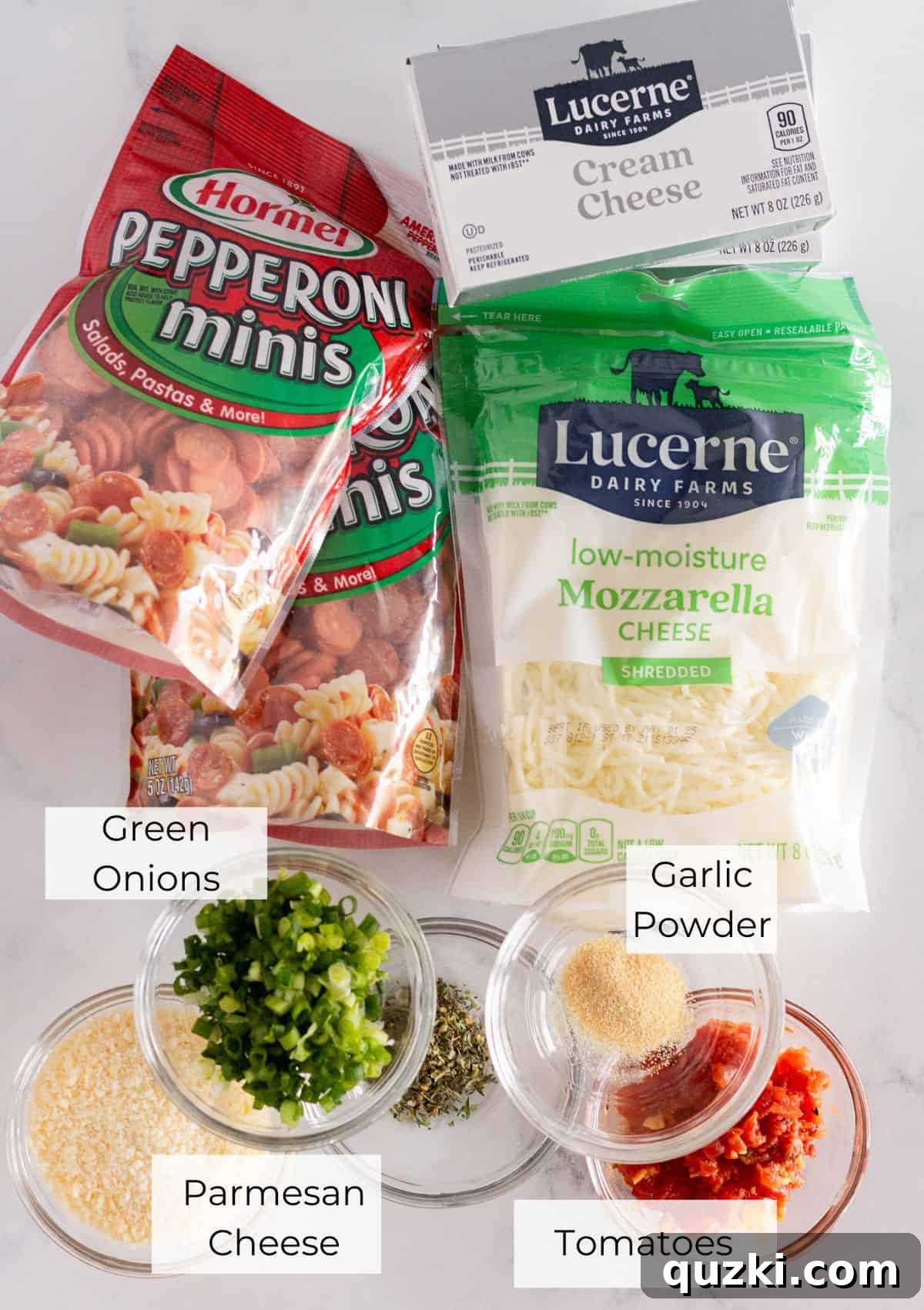 Touchdown Pizza Cheese Ball 3 All the essential ingredients for making the football pepperoni pizza cheese ball are neatly arranged on a white surface. These include blocks of cream cheese, Italian seasoning, shredded mozzarella and parmesan cheeses, a bowl of petite diced tomatoes, sliced green onions, and mini pepperoni.