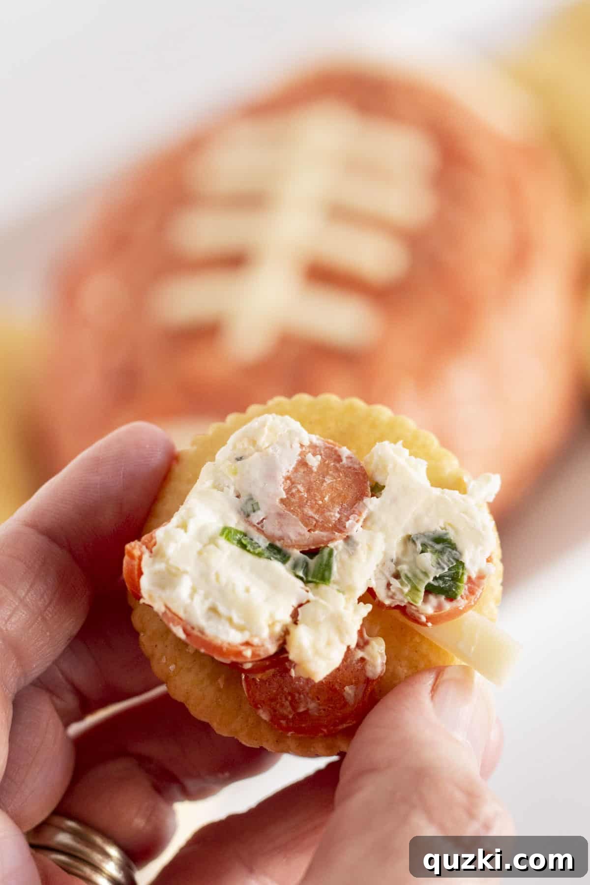 Touchdown Pizza Cheese Ball 7 A crisp cracker expertly topped with a generous, enticing scoop of the pepperoni pizza football cheese ball, showcasing its rich texture and flavorful inclusions, poised for an enjoyable bite.