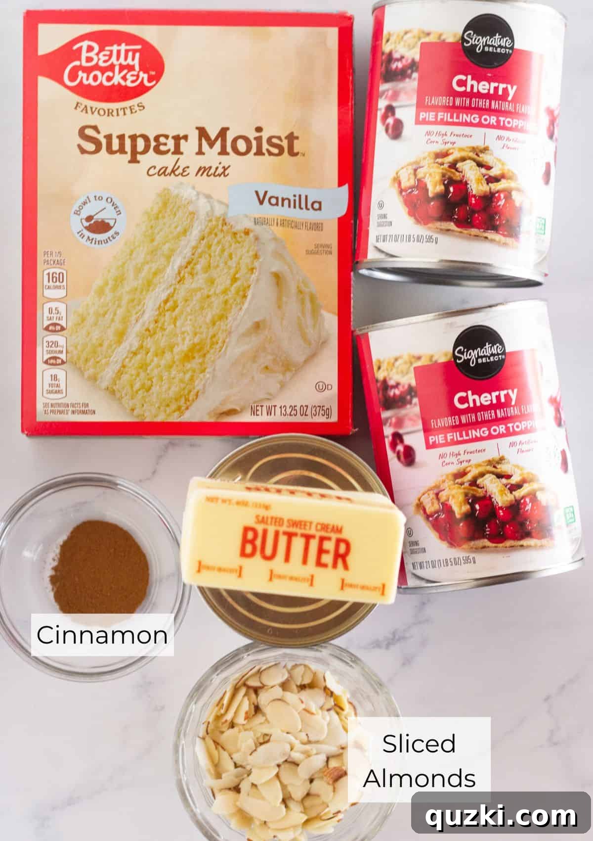 The five essential ingredients laid out for making cherry cobbler with a cake mix: cherry pie filling, vanilla cake mix, cinnamon, sliced almonds, and butter.