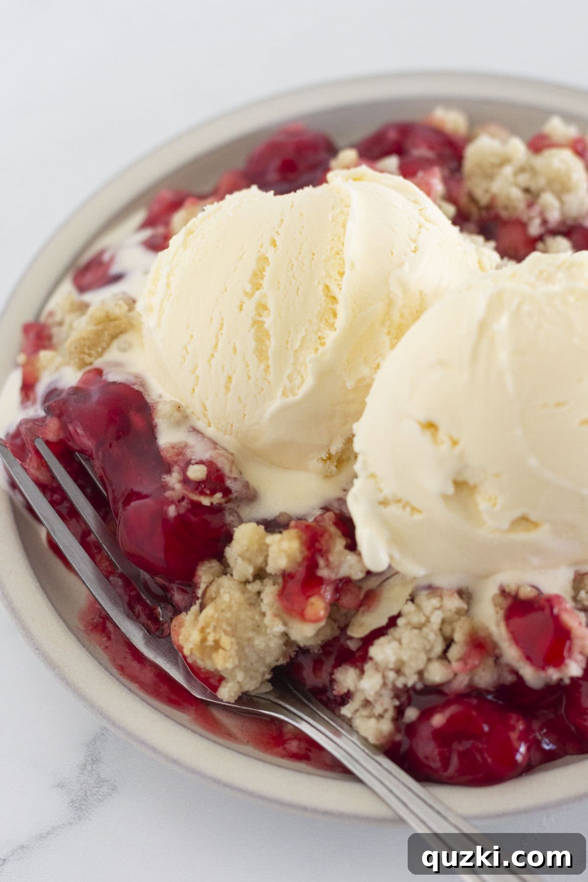A generous serving of cherry cobbler made with a cake mix, topped with melting vanilla ice cream and a spoon.