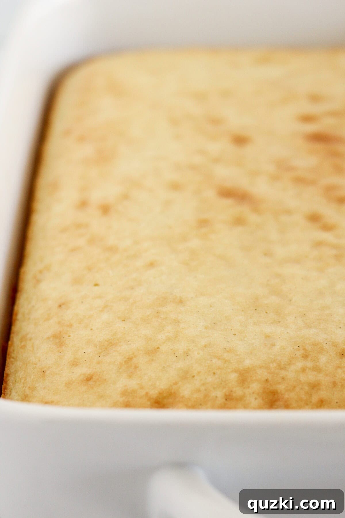 Perfect Vanilla Sheet Cake 6 A freshly baked vanilla sheet cake in a white baking dish, golden brown on top.
