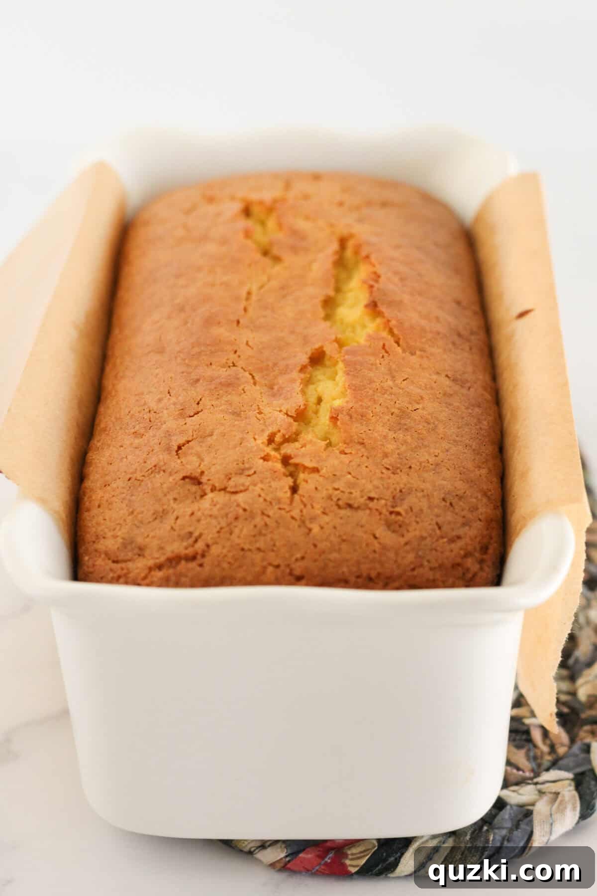 Sunshine Lemon Loaf 6 A freshly baked lemon loaf, golden brown and cooling in its white ceramic loaf pan, infused with citrus aroma.