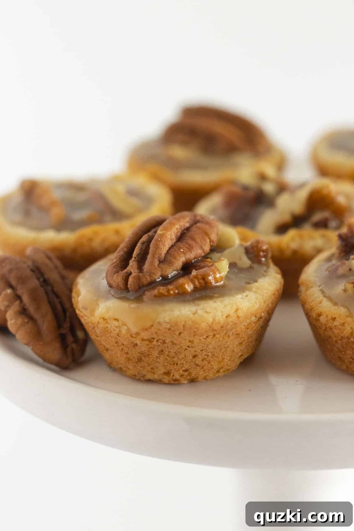 A white cake plate adorned with several golden Pecan Pie Cookie Bites, highlighting their inviting texture and rich color.