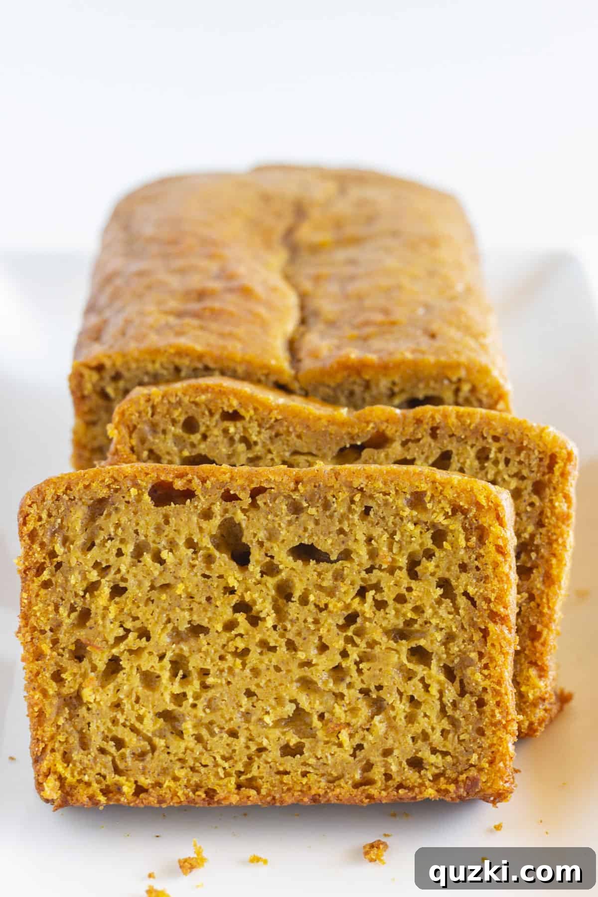 A whole loaf of Pumpkin Spice Bread with two perfectly sliced pieces, showcasing its moist crumb.