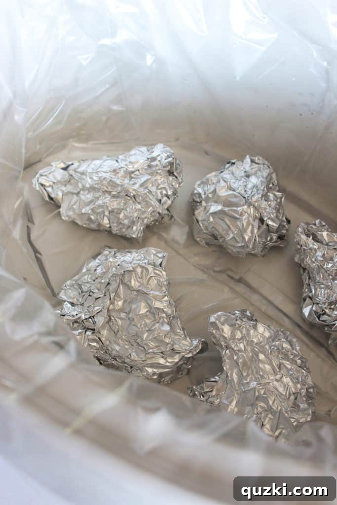 Foil balls and liquid placed at the bottom of a slow cooker.