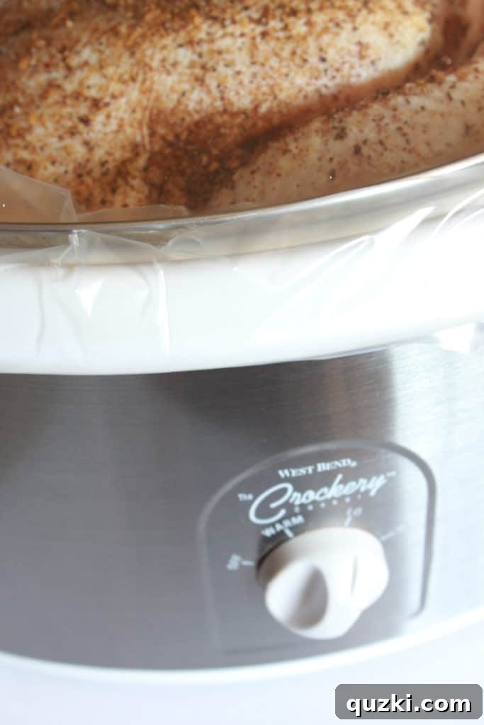 Whole chicken resting on foil balls in a slow cooker, covered and cooking.