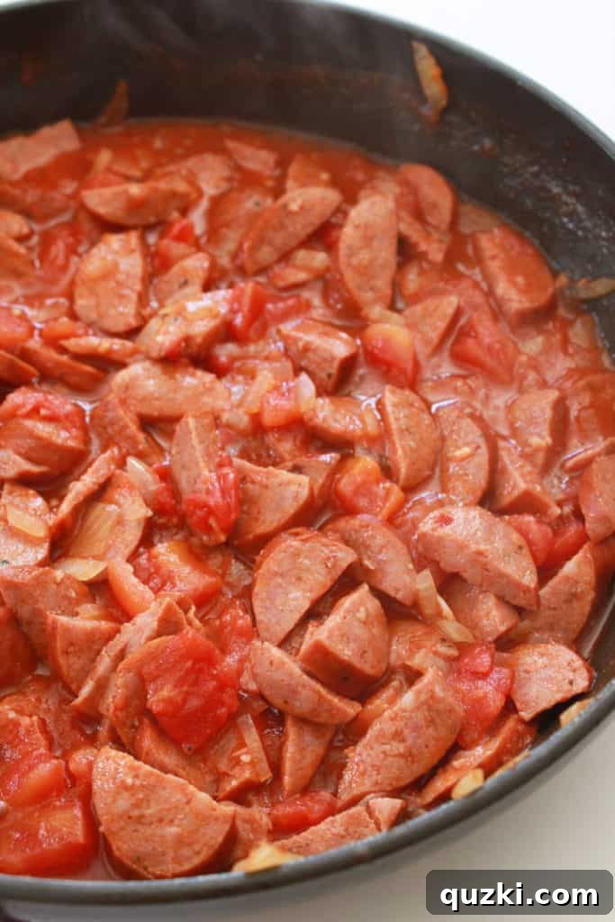 Fast and Flavorful 15-Minute Andouille Sausage Grits 5 Petite diced tomatoes and Cajun seasoning being added to the pan with browned Andouille sausage, onions, and garlic, creating a vibrant sauce base.