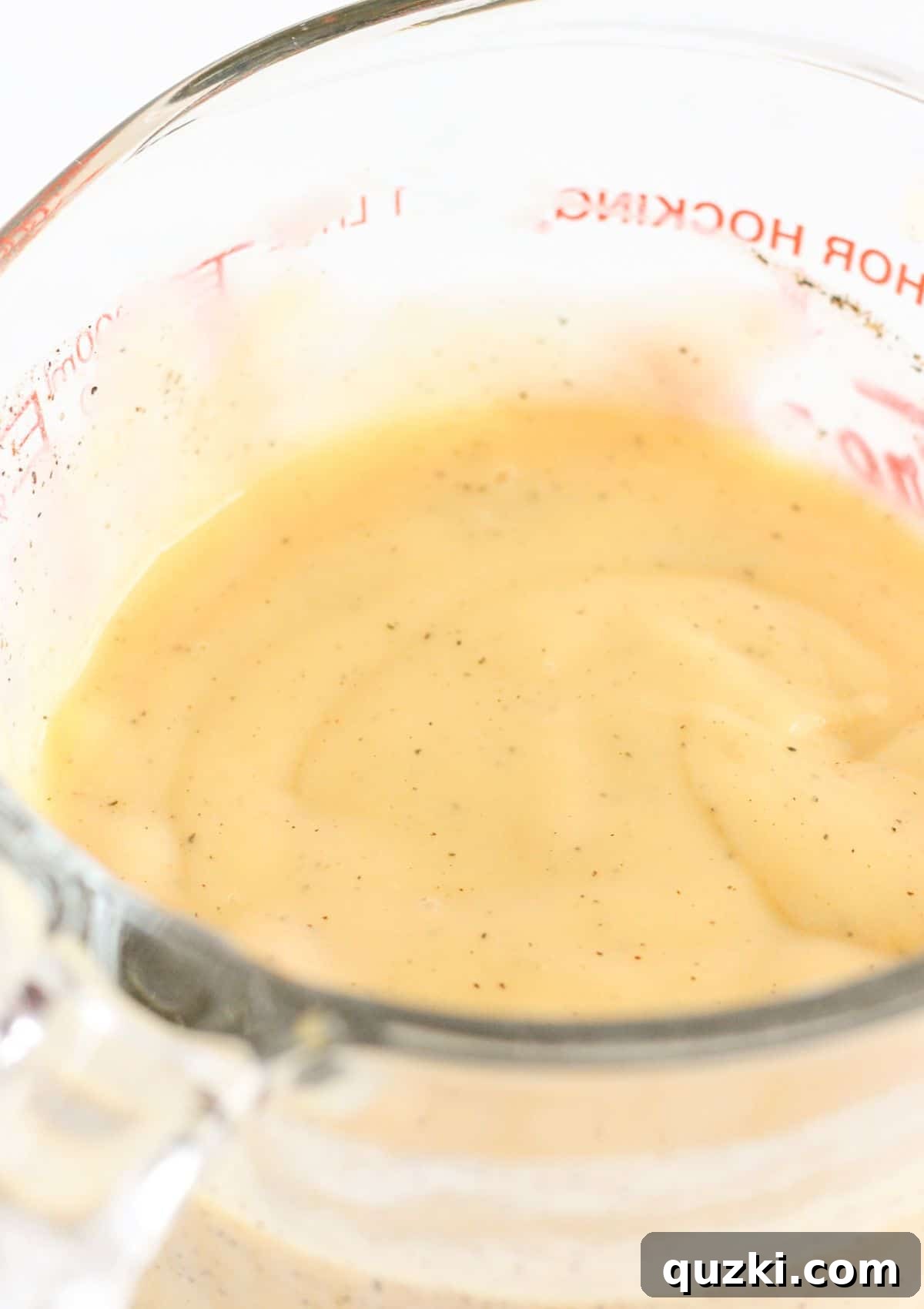 A bowl containing cream of chicken soup and milk, whisked together to form a smooth, creamy sauce.