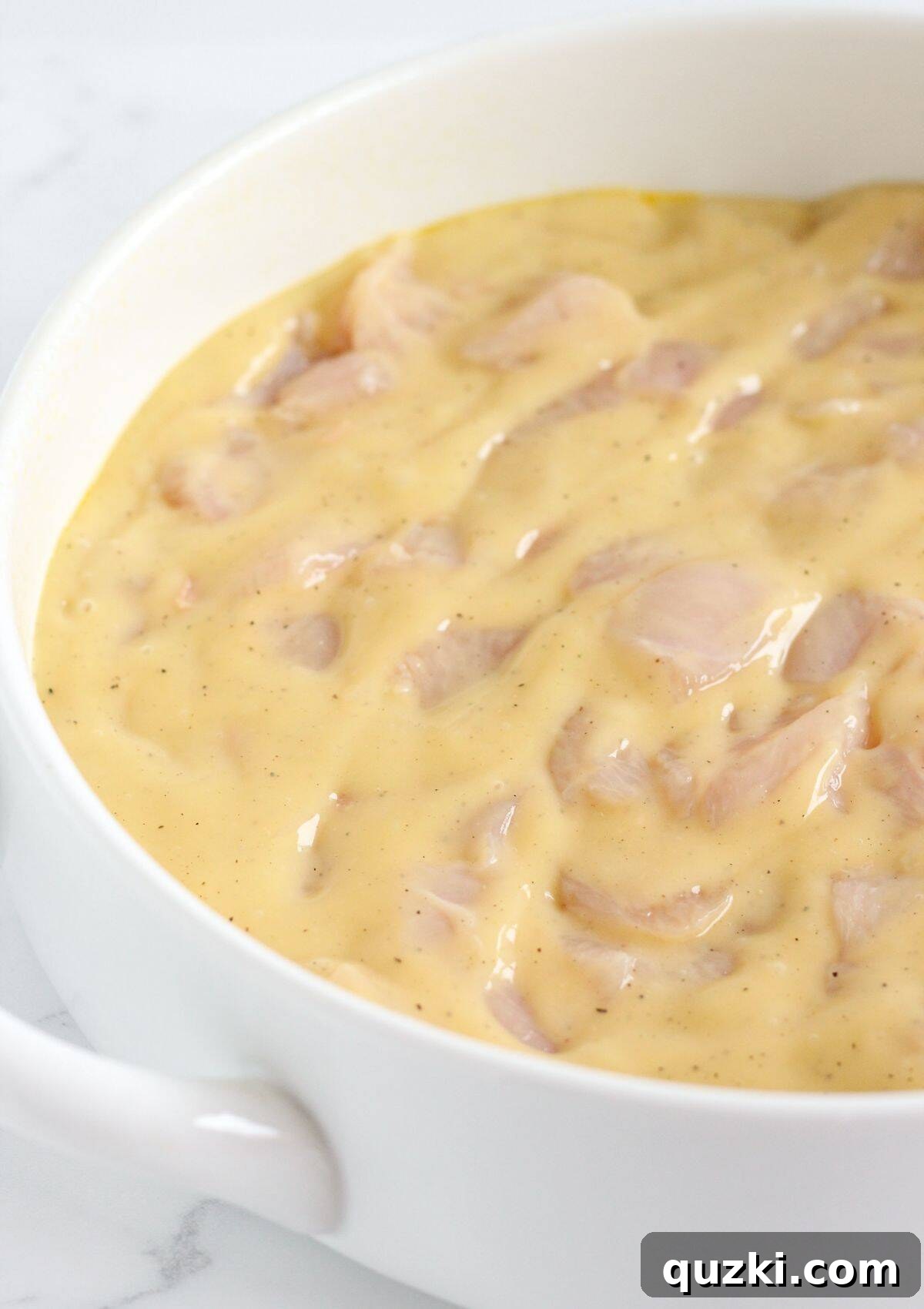 Bite-sized chicken pieces mixed with the creamy soup sauce, being poured into the prepared casserole dish.