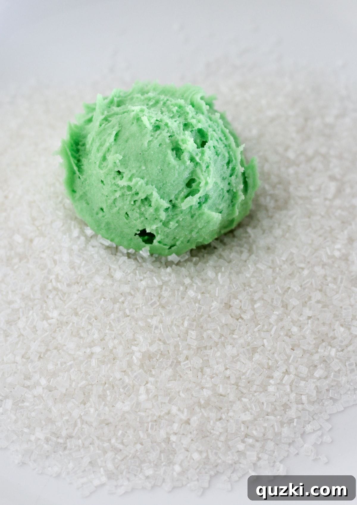 Rolling a ball of green cookie dough in sanding sugar.