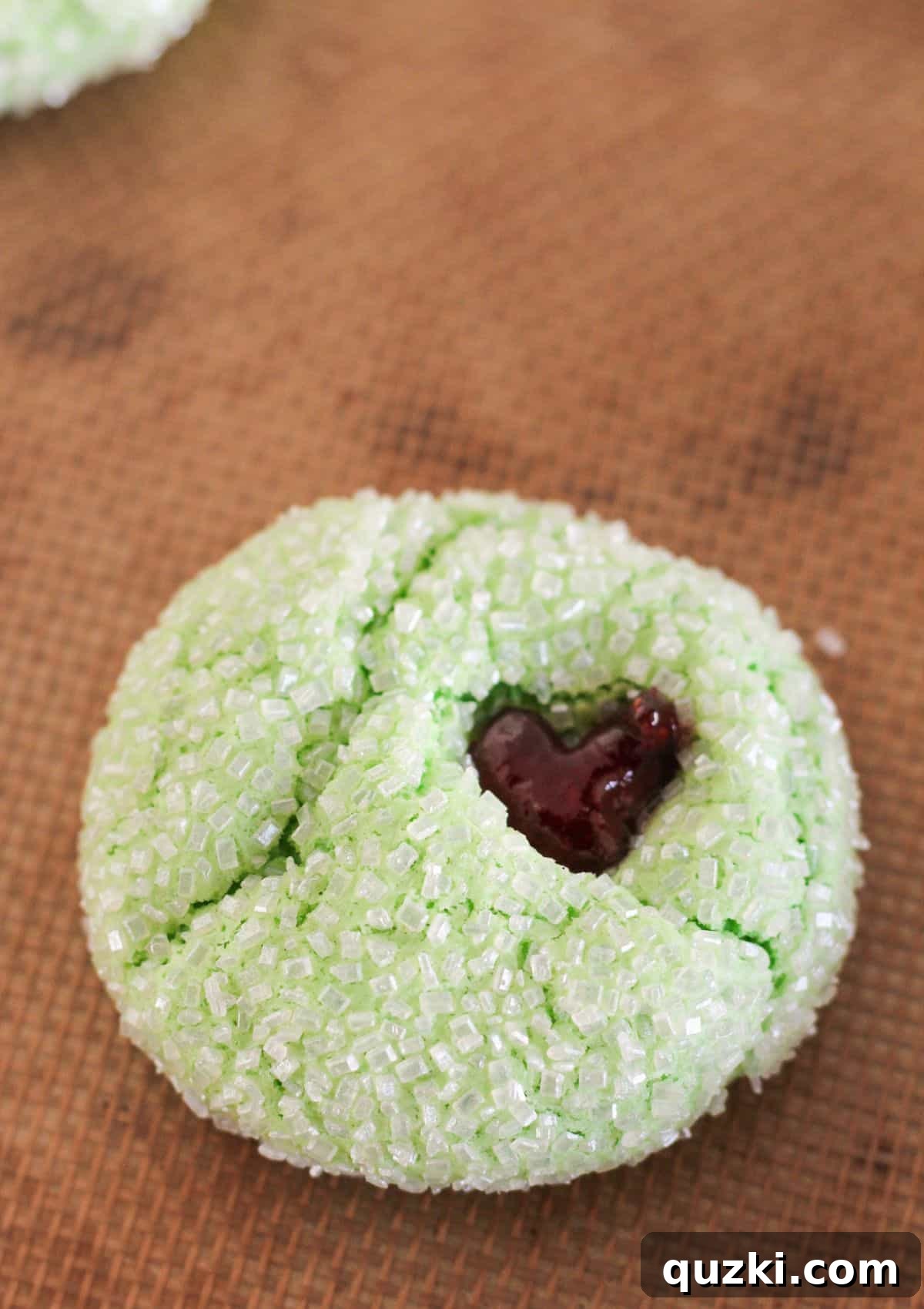 Filling the heart indentation of a green cookie with bright red raspberry jam.