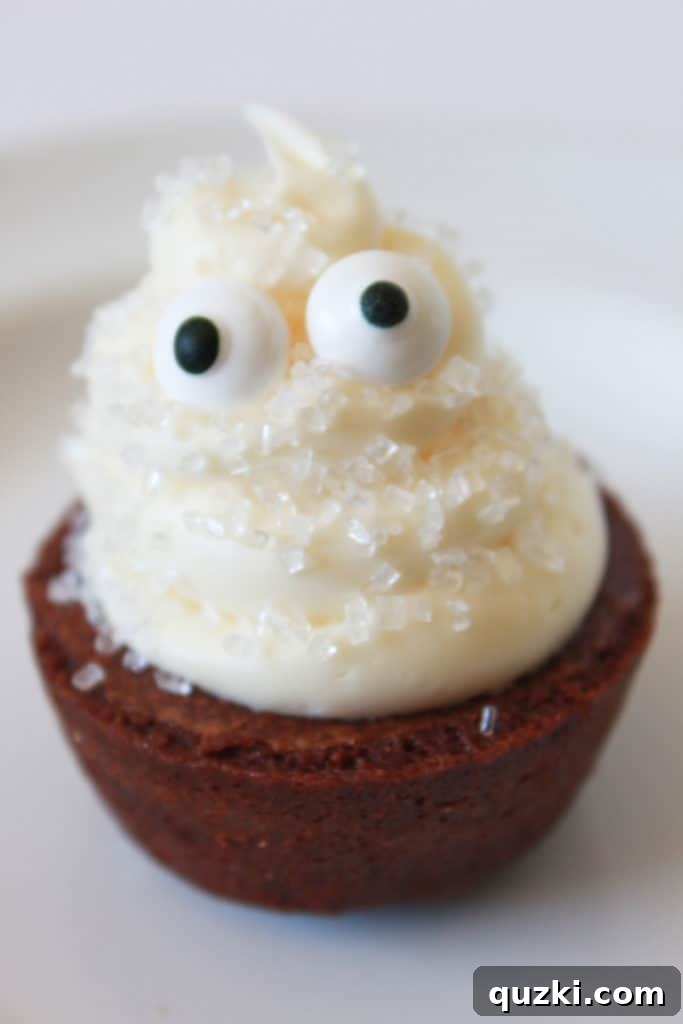 Ghoulishly Good Halloween Brownie Bites 4 Close-up of a Ghost Halloween Brownie Bite, featuring a tall swirl of vanilla frosting and two edible eyeballs, on a white background.